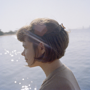 A portrait photo of me, Laurel Schwulst — I'm a white woman in my early 30s with short brown hair seen in portrait silhoutte mode — the left side of my face smiles while looking outwards to the ocean, the sun glimmering behind me. The photograph was taken by Jason Fulford at 7am on 7-7-21.